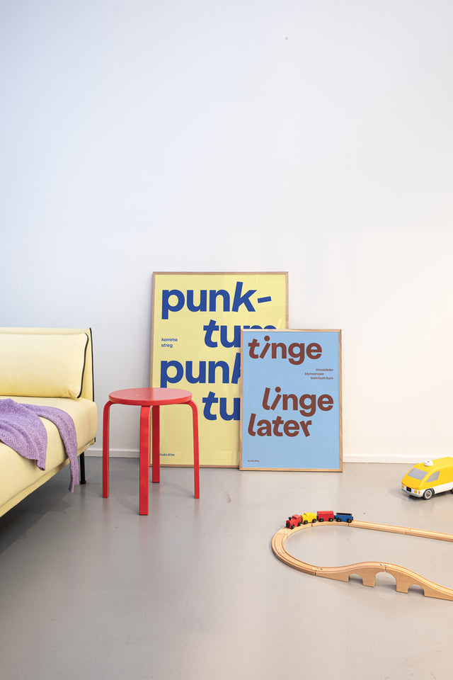 Gul "punktum punktum" børneplakat og lyseblå "tinge-linge-later" børneplakat på børneværelse med gul sofa